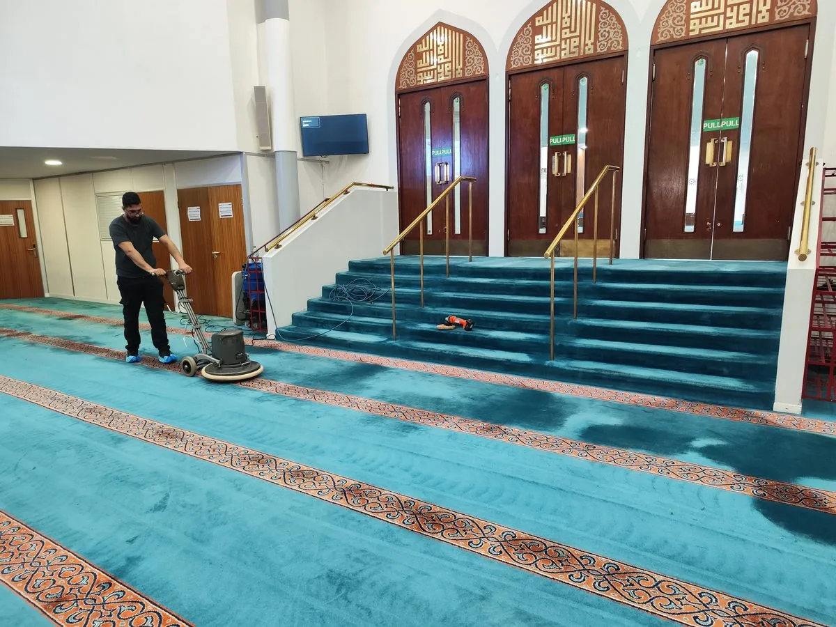 Rotary machine cleaning the turquoise prayer hall carpet of a London mosque