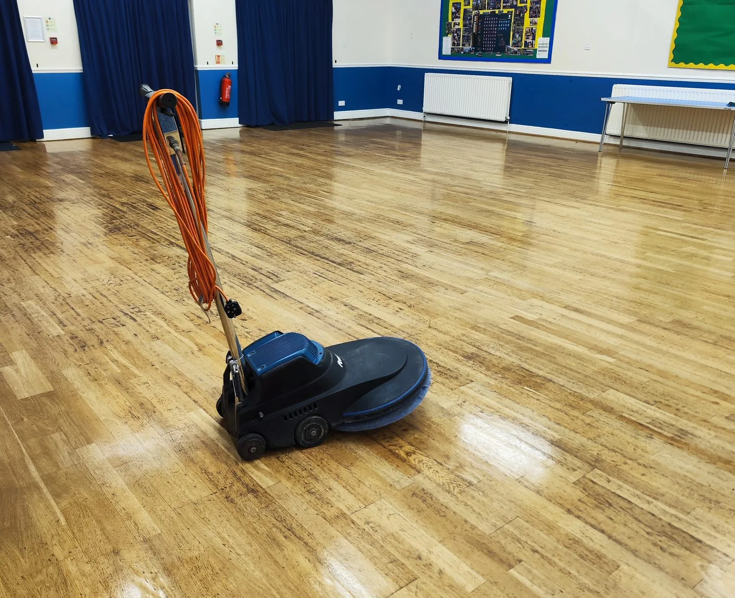 Rotary buffer restoring the wood floor of a community hall